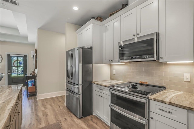 kitchen featuring visible vents, light wood-style flooring, stainless steel appliances, white cabinets, and backsplash