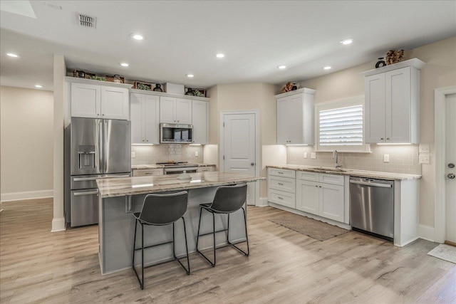 kitchen featuring visible vents, a sink, a kitchen island, appliances with stainless steel finishes, and light stone countertops