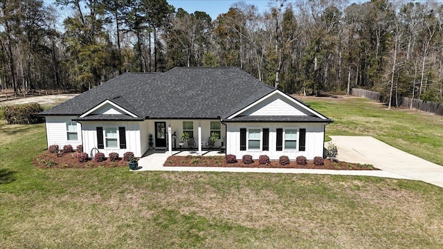 modern inspired farmhouse with a front yard, fence, roof with shingles, and a view of trees