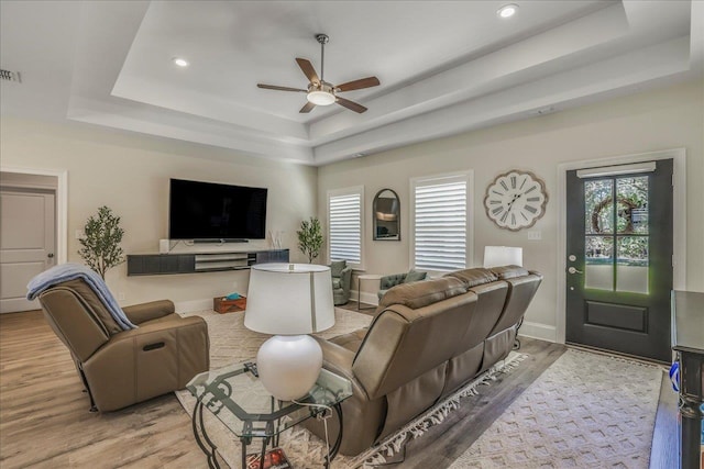 living room featuring light wood finished floors, ceiling fan, baseboards, and a tray ceiling