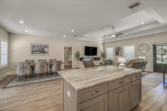 kitchen with baseboards, visible vents, a kitchen island, light wood-style floors, and a raised ceiling