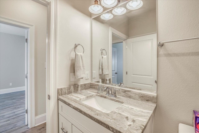 half bathroom featuring vanity, baseboards, and wood finished floors