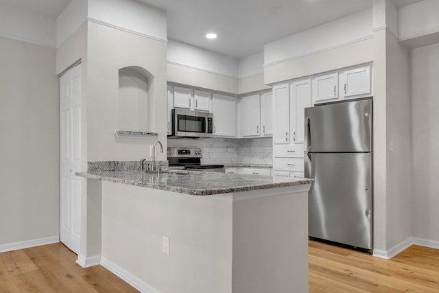 kitchen with kitchen peninsula, appliances with stainless steel finishes, light wood-type flooring, and white cabinets