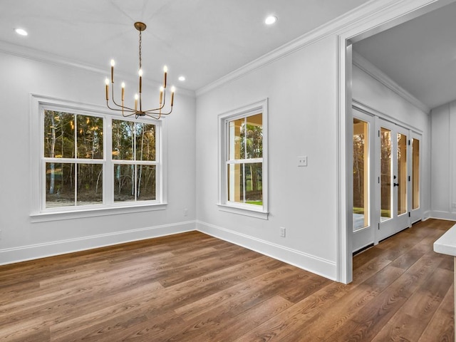 unfurnished dining area featuring dark wood-type flooring, crown molding, a healthy amount of sunlight, and an inviting chandelier