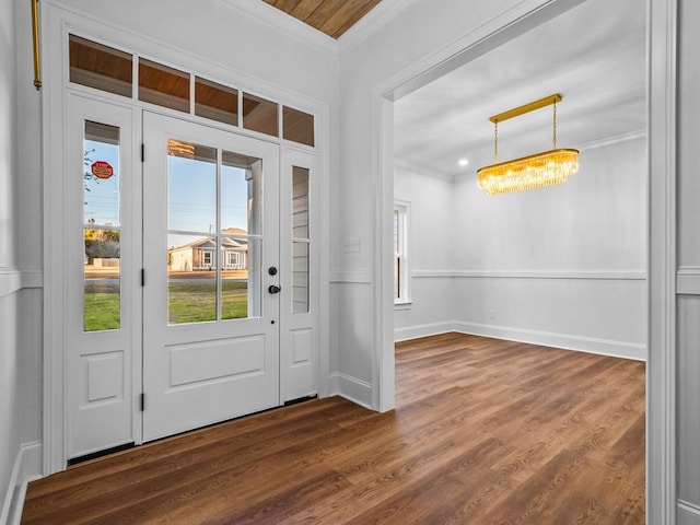 foyer entrance featuring dark wood-type flooring, ornamental molding, and a chandelier