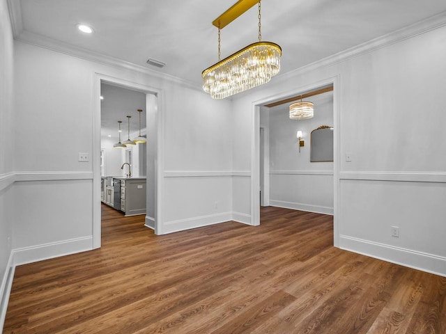 unfurnished dining area featuring sink, dark hardwood / wood-style floors, crown molding, and a chandelier