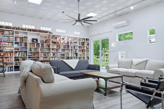 living room with ceiling fan, a wall unit AC, light hardwood / wood-style floors, and a towering ceiling