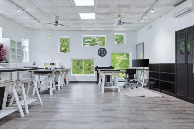 office with a towering ceiling, a wall unit AC, wood-type flooring, and ceiling fan