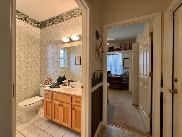 ensuite bathroom featuring connected bathroom, tile patterned flooring, wallpapered walls, toilet, and vanity