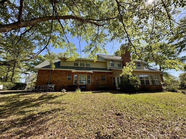 back of house featuring brick siding and a lawn