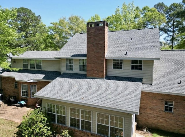 back of property with a shingled roof, a patio area, and a chimney