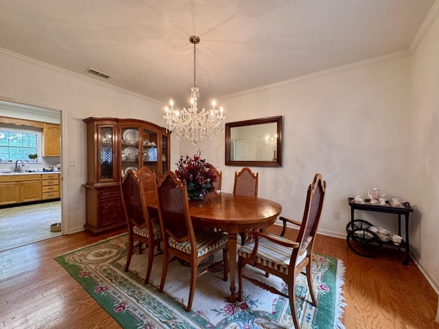 dining area featuring an inviting chandelier, visible vents, crown molding, and light wood-style flooring