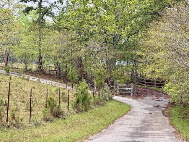 view of property's community with fence, driveway, and a view of trees