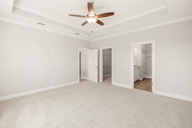 unfurnished bedroom featuring a tray ceiling, a spacious closet, ceiling fan, and ensuite bathroom