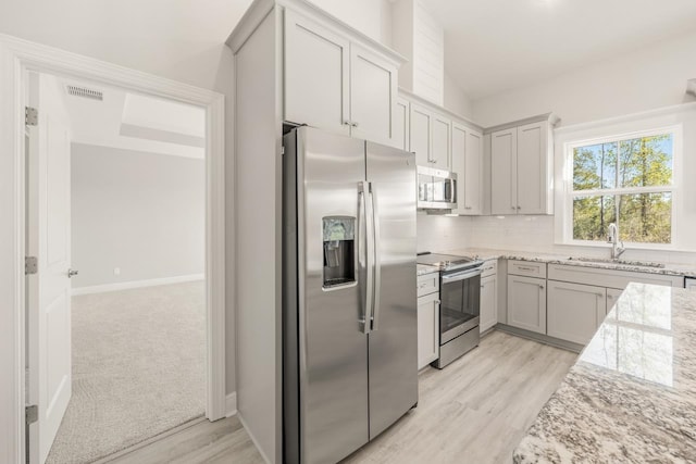 kitchen featuring sink, stainless steel appliances, light carpet, light stone counters, and decorative backsplash