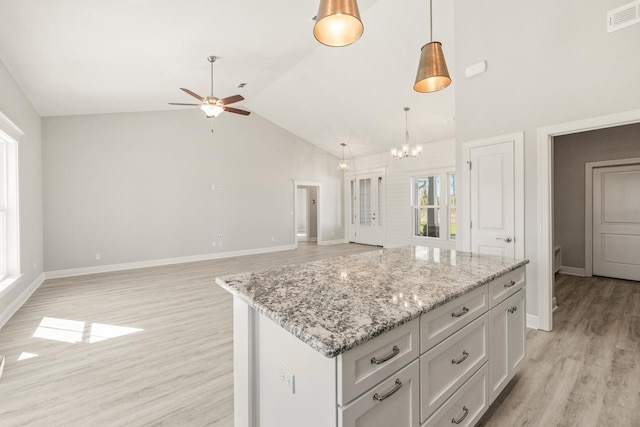 kitchen with ceiling fan with notable chandelier, light hardwood / wood-style flooring, light stone countertops, decorative light fixtures, and a kitchen island