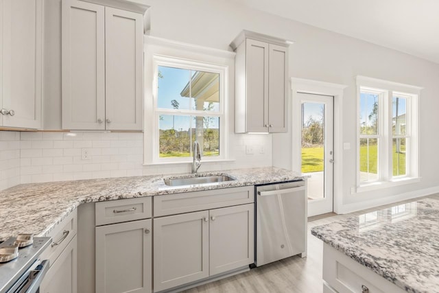 kitchen with sink, stainless steel dishwasher, light stone countertops, tasteful backsplash, and light hardwood / wood-style floors