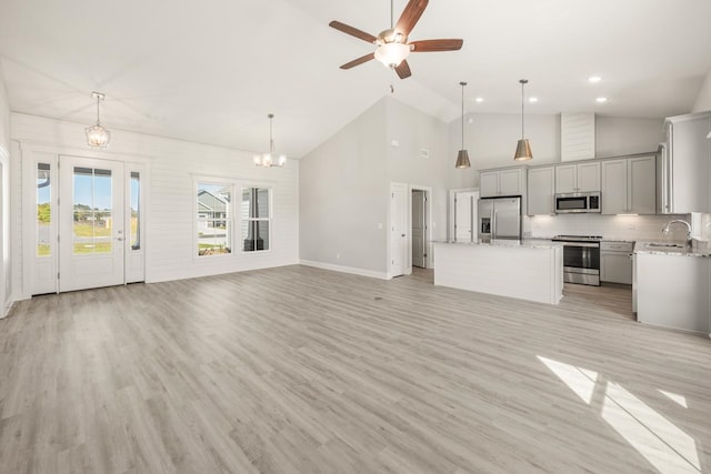 unfurnished living room with ceiling fan with notable chandelier, light hardwood / wood-style floors, sink, and high vaulted ceiling