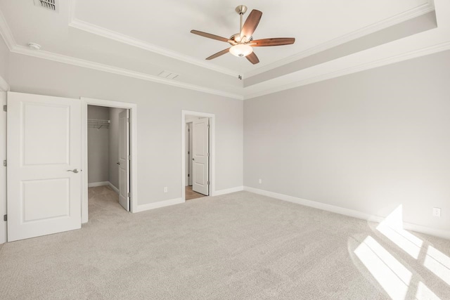 unfurnished bedroom with ceiling fan, a spacious closet, crown molding, and a tray ceiling