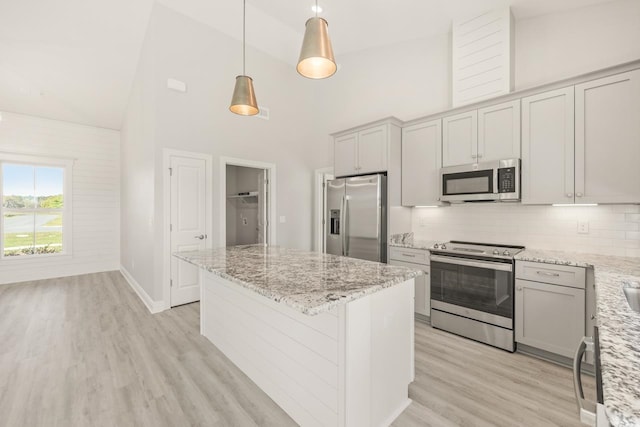 kitchen featuring tasteful backsplash, light stone counters, stainless steel appliances, decorative light fixtures, and high vaulted ceiling