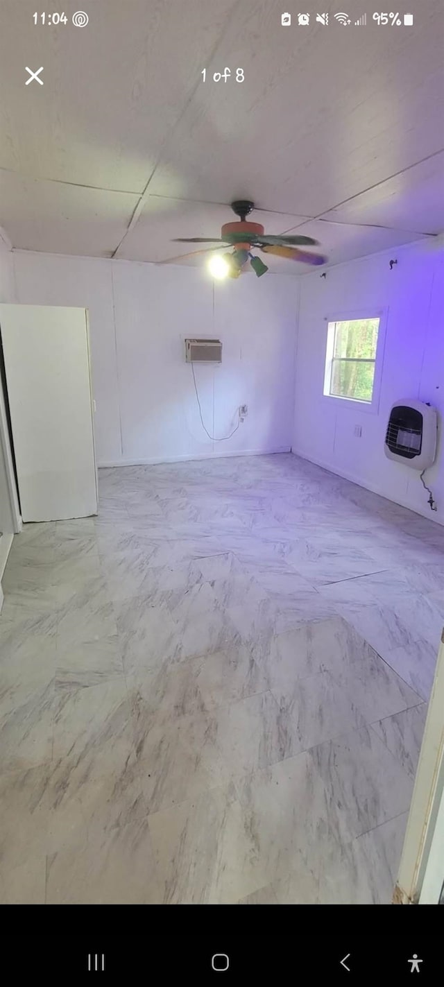 unfurnished room with heating unit, marble finish floor, and a ceiling fan