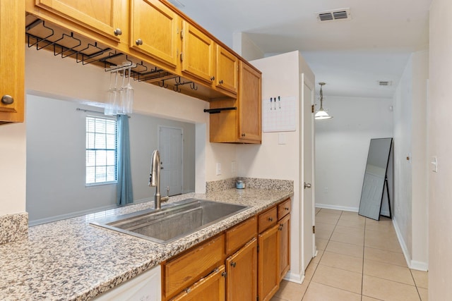 kitchen featuring sink, light tile patterned flooring, light stone counters, and hanging light fixtures