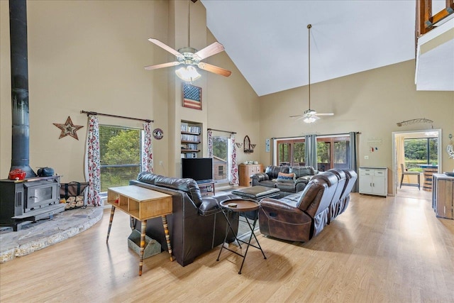 living room with high vaulted ceiling, light wood-type flooring, a wood stove, and ceiling fan
