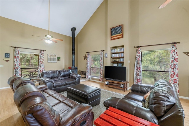 living room featuring a wood stove, a healthy amount of sunlight, light wood-type flooring, and high vaulted ceiling