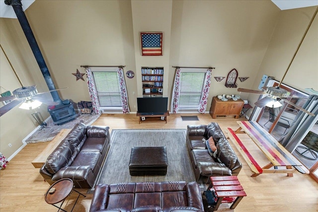 living room featuring hardwood / wood-style floors, a towering ceiling, ceiling fan, and a wood stove