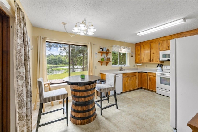 kitchen featuring decorative light fixtures, a textured ceiling, sink, a kitchen breakfast bar, and white appliances