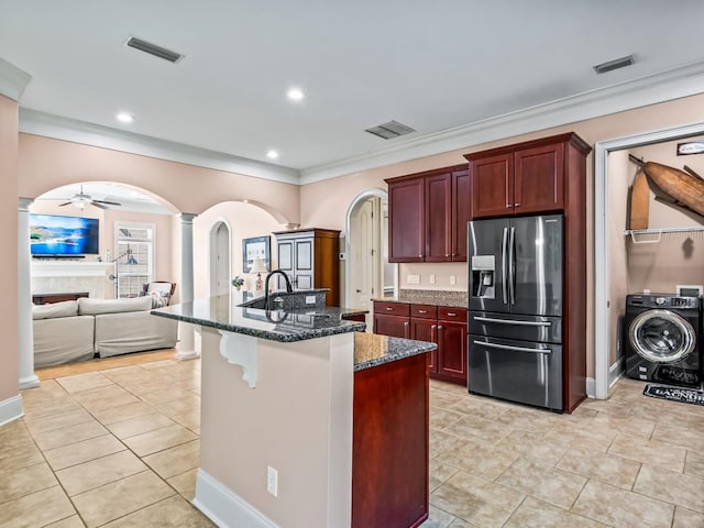 kitchen featuring ornate columns, dark stone counters, an island with sink, stainless steel fridge with ice dispenser, and washer / dryer