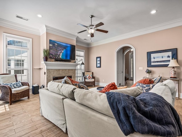 living room featuring ornamental molding, ceiling fan, a tile fireplace, and light hardwood / wood-style floors