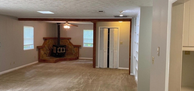 unfurnished living room featuring a textured ceiling, light carpet, a wood stove, and a wealth of natural light