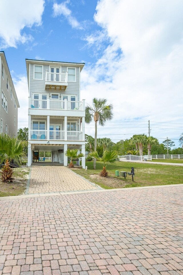 coastal home featuring a front yard, a balcony, and a carport