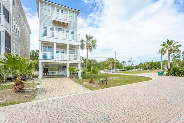 coastal inspired home with a front yard, a balcony, and a carport