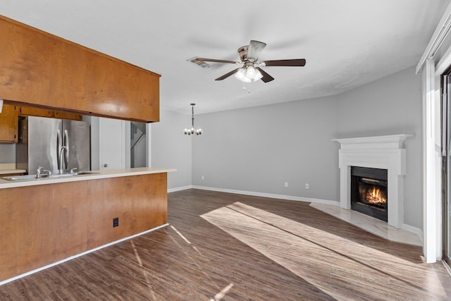 kitchen featuring hanging light fixtures, dark hardwood / wood-style flooring, ceiling fan with notable chandelier, stainless steel refrigerator, and sink