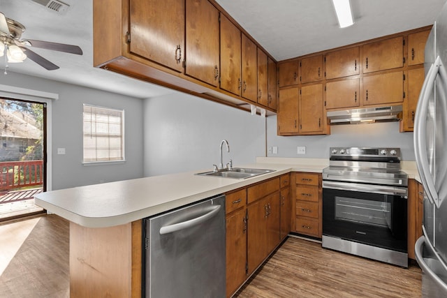 kitchen with kitchen peninsula, light wood-type flooring, appliances with stainless steel finishes, ceiling fan, and sink