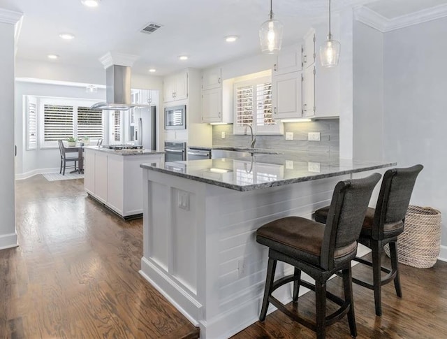 kitchen featuring island exhaust hood, visible vents, appliances with stainless steel finishes, a sink, and a peninsula