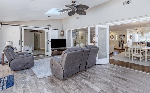 living room with ceiling fan with notable chandelier, wood finished floors, visible vents, and a barn door