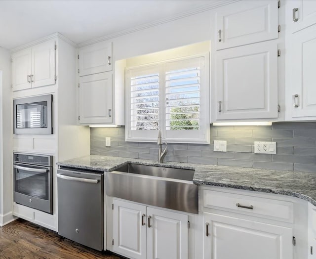 kitchen with light stone counters, decorative backsplash, appliances with stainless steel finishes, white cabinets, and a sink