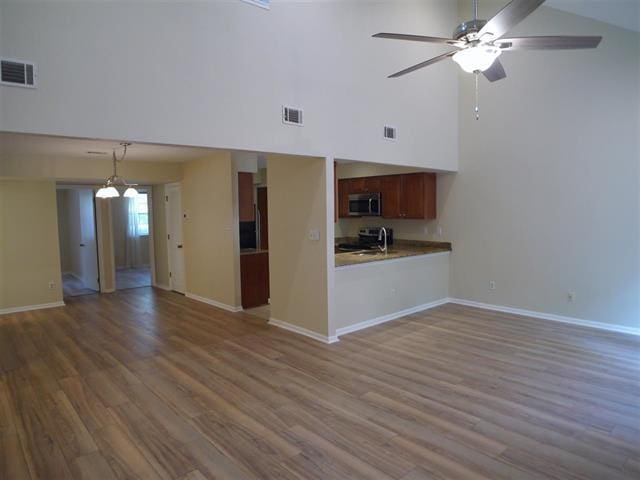 unfurnished living room featuring hardwood / wood-style floors, ceiling fan, and a towering ceiling