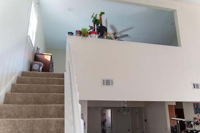 stairs featuring ceiling fan with notable chandelier and a high ceiling