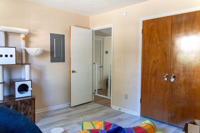 bedroom featuring a closet, a textured ceiling, electric panel, and light hardwood / wood-style flooring