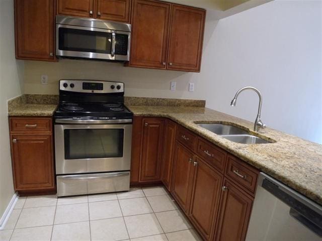 kitchen with sink, light stone countertops, appliances with stainless steel finishes, light tile patterned flooring, and kitchen peninsula