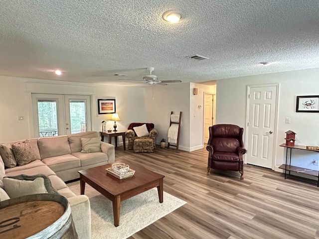 living area with a textured ceiling, visible vents, ceiling fan, wood finished floors, and french doors