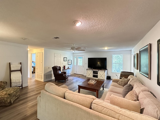 living area with dark wood-type flooring, a textured ceiling, visible vents, and a ceiling fan