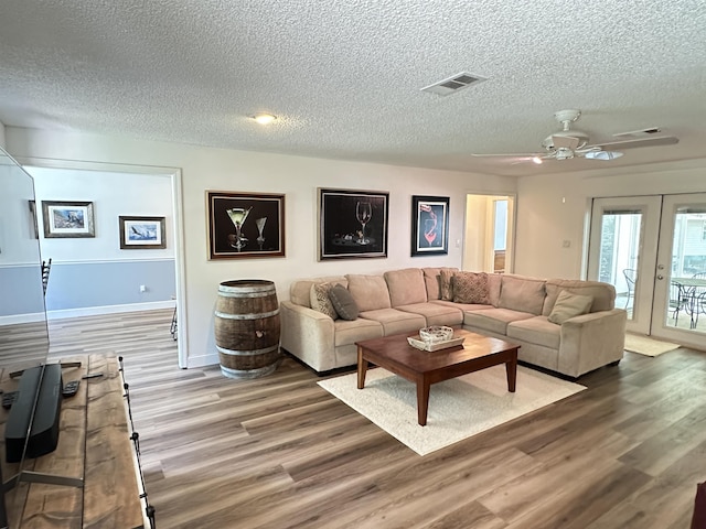 living room featuring french doors, a textured ceiling, visible vents, ceiling fan, and wood finished floors