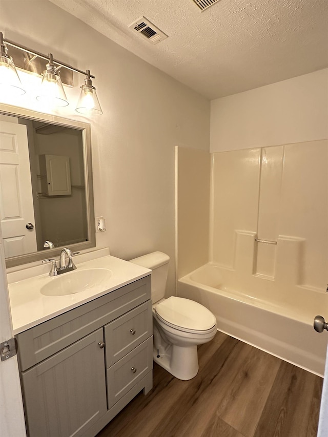 bathroom featuring a textured ceiling, visible vents, toilet, wood finished floors, and vanity