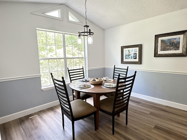 dining space with a textured ceiling, dark wood-style flooring, vaulted ceiling, and an inviting chandelier