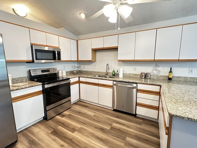 kitchen featuring stainless steel appliances, a textured ceiling, a sink, white cabinets, and wood finished floors